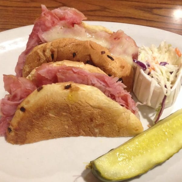 A Main Bar Sandwich Shop sandwich with meat and cheese, coleslaw, and a pickle spear.