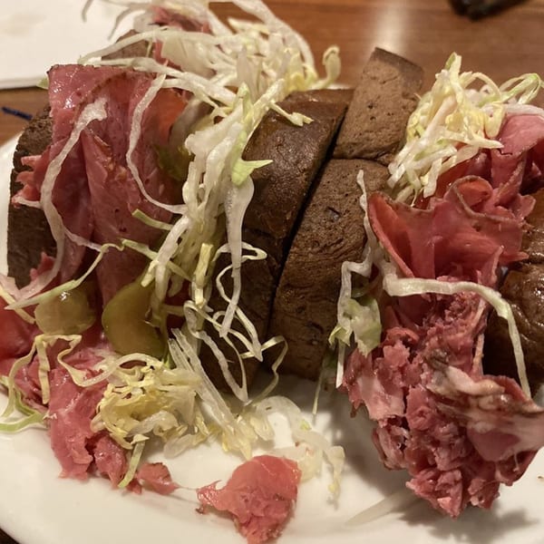 A Main Bar Sandwich Shop pastrami sandwich on dark bread with shredded lettuce and pickles.