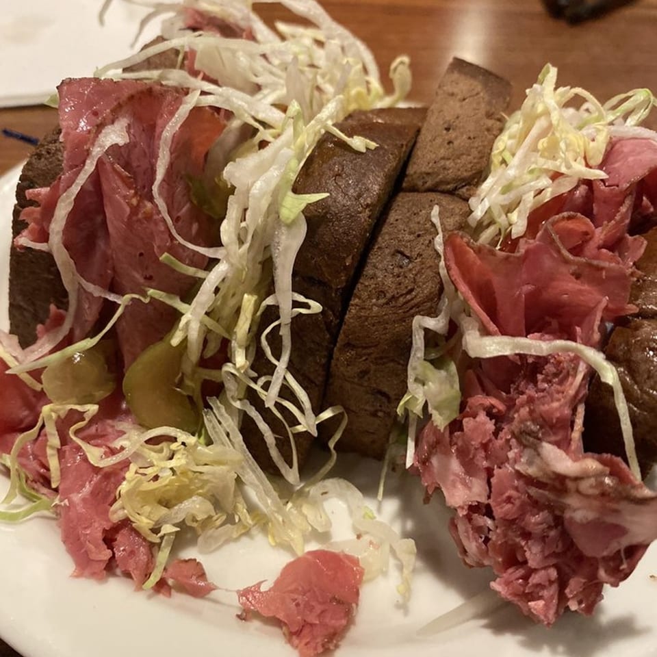 A Main Bar Sandwich Shop pastrami sandwich on dark bread with shredded lettuce and pickles.