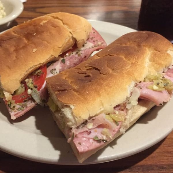 Two Main Bar Sandwich Shop sandwiches on a white plate, filled with meat, cheese, and vegetables.