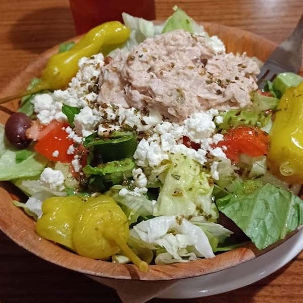 A fresh tuna salad with lettuce, tomatoes, feta cheese, olives, and yellow peppers in a wooden bowl.